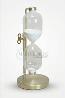 Clear glass hourglass with gold detailing placed on a wooden side table in a sophisticated interior.