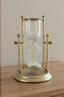 Medium clear glass and gold sand timer displayed on a marble coffee table in a modern living room.