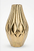 Tall golden metal vase placed beside a living room accent chair in a modern interior.
